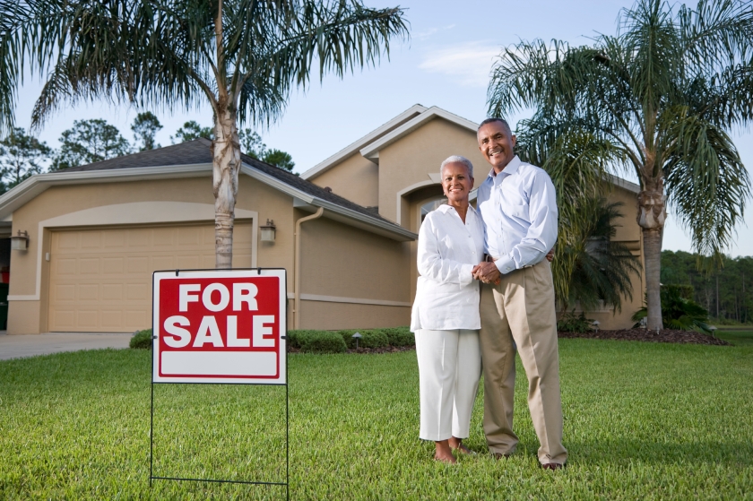 Happy African American couple outside house with for sale sign